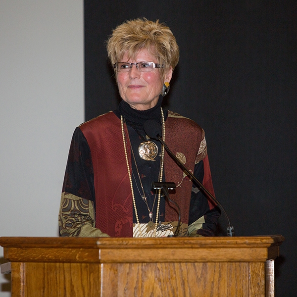 A photo of Katee Tully, wearing a garnet vest and black shirt, standing at a podium