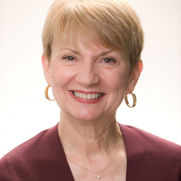 A headshot of Stella Cottrell, smiling, wearing a garnet blouse