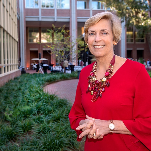 A photo of Dr. Coburn wearing a red dress, standing outside with her hands folded, smiling