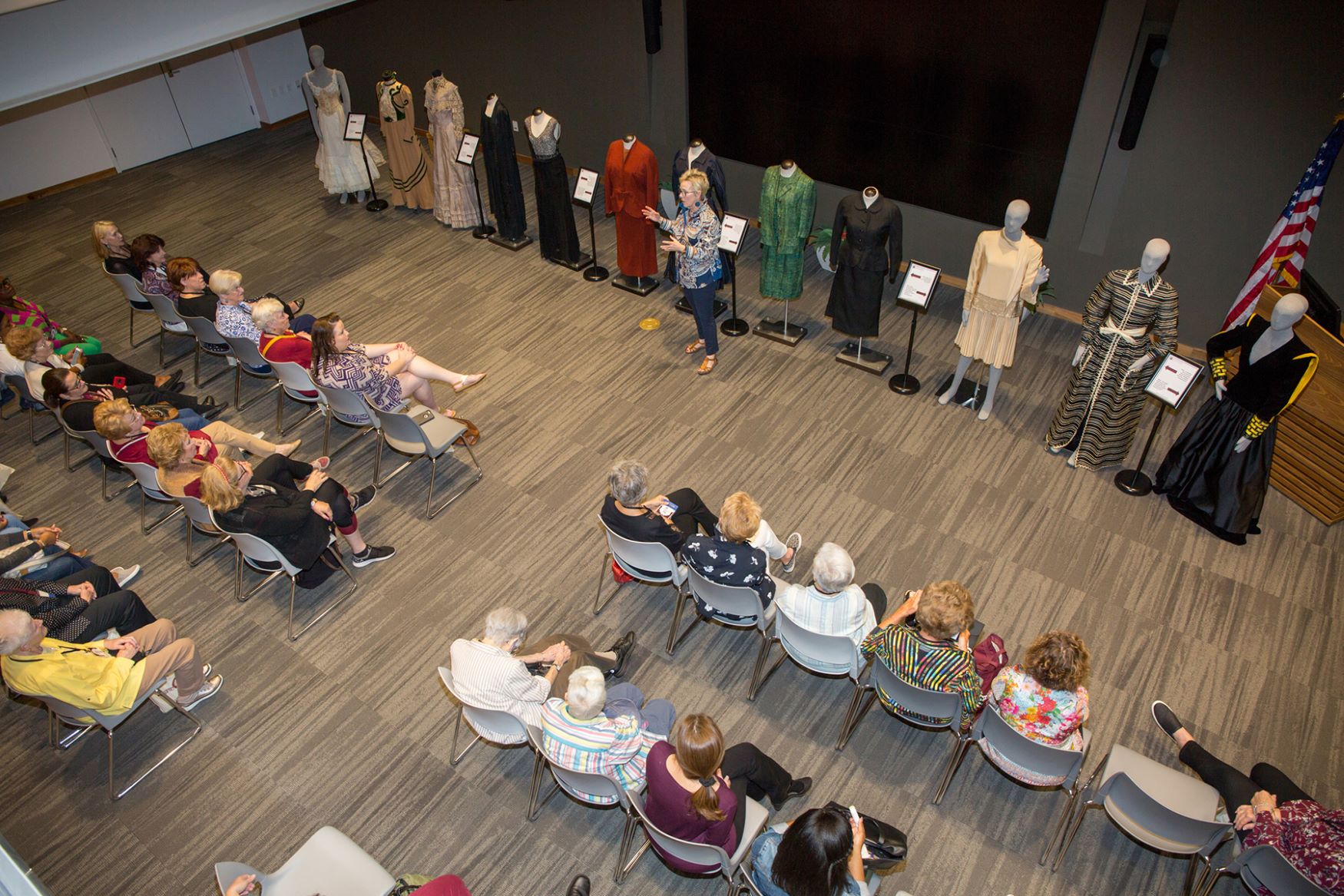 An overhead photo of a woman presenting various styles of clothing on mannequins to an audience