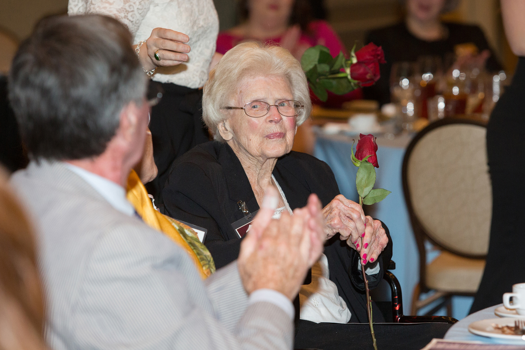 A photo of an elderly women holding a red rose